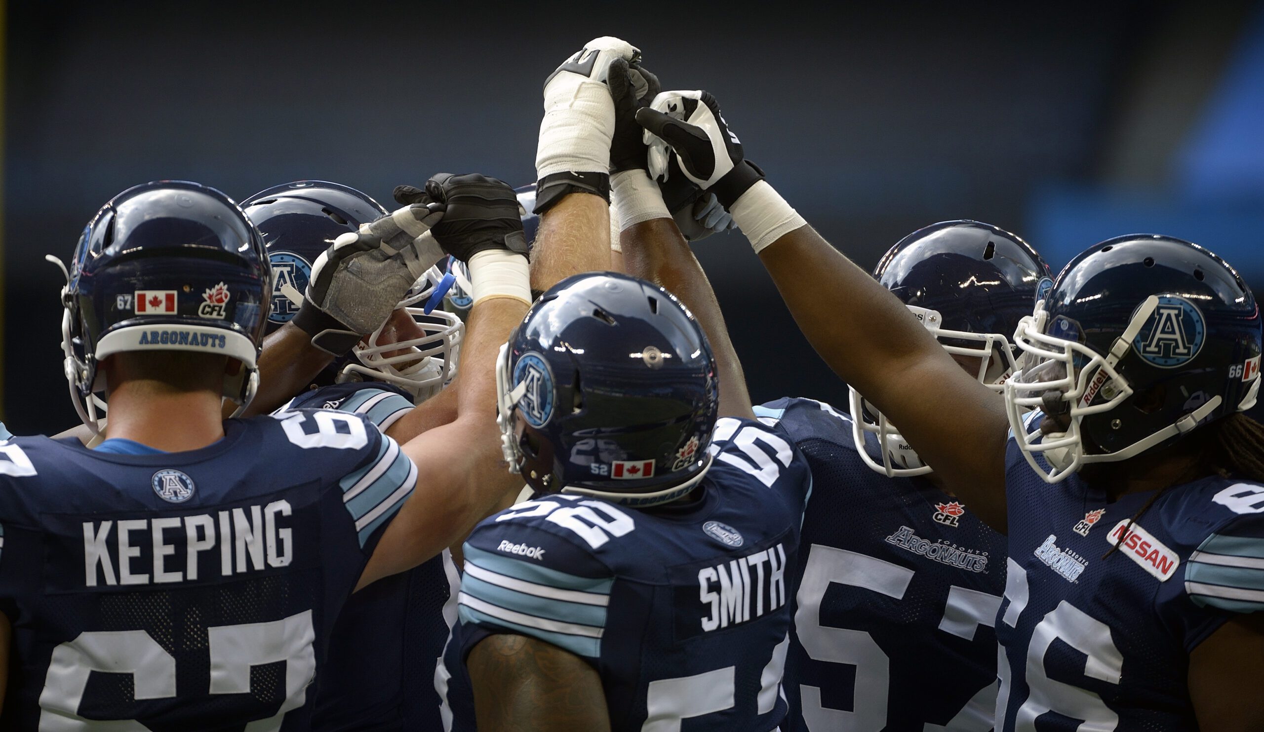 A group of football players in navy blue uniforms in a huddle.