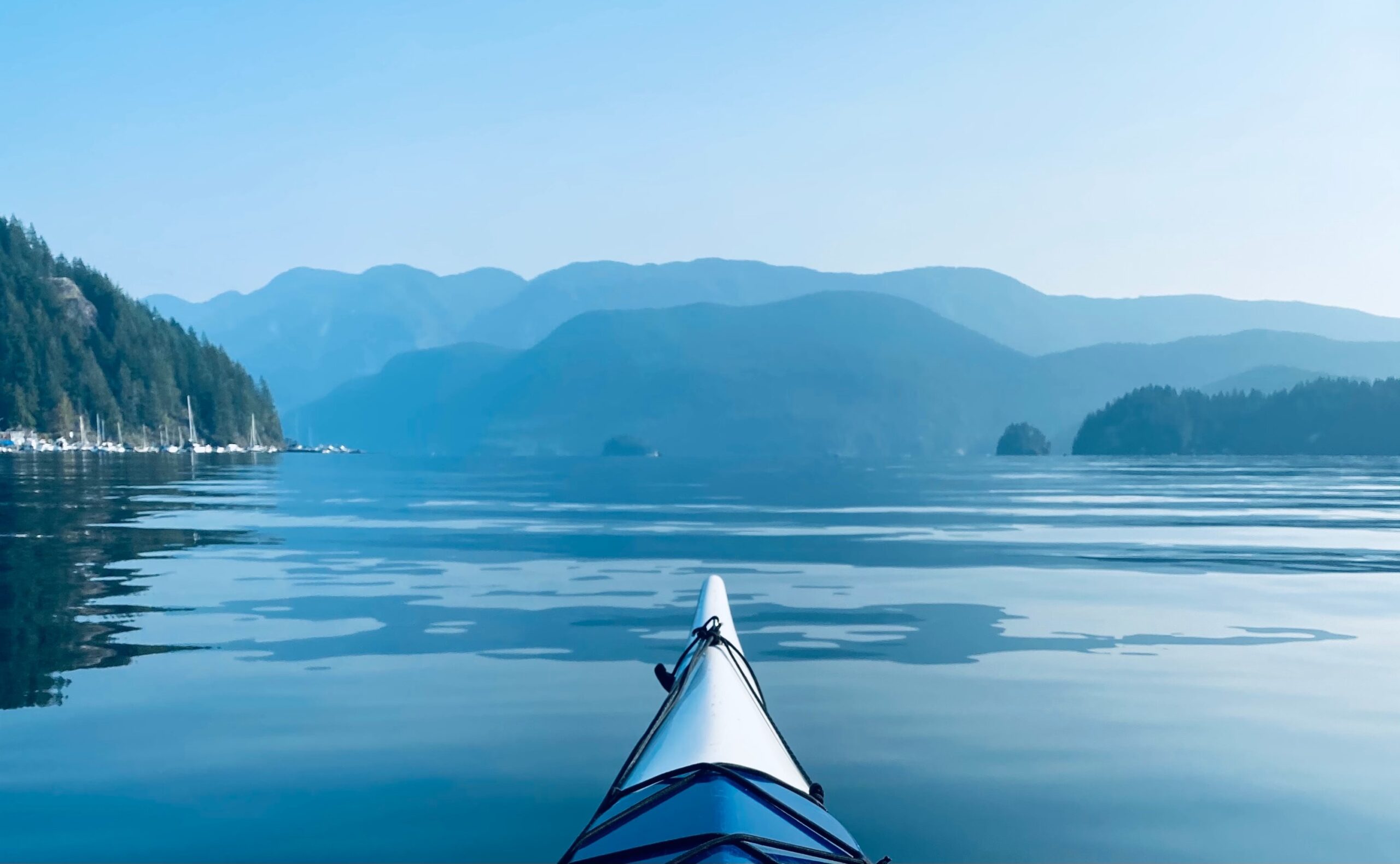 The front end of a kayak in a body of water in front of mountains in North Vancouver.