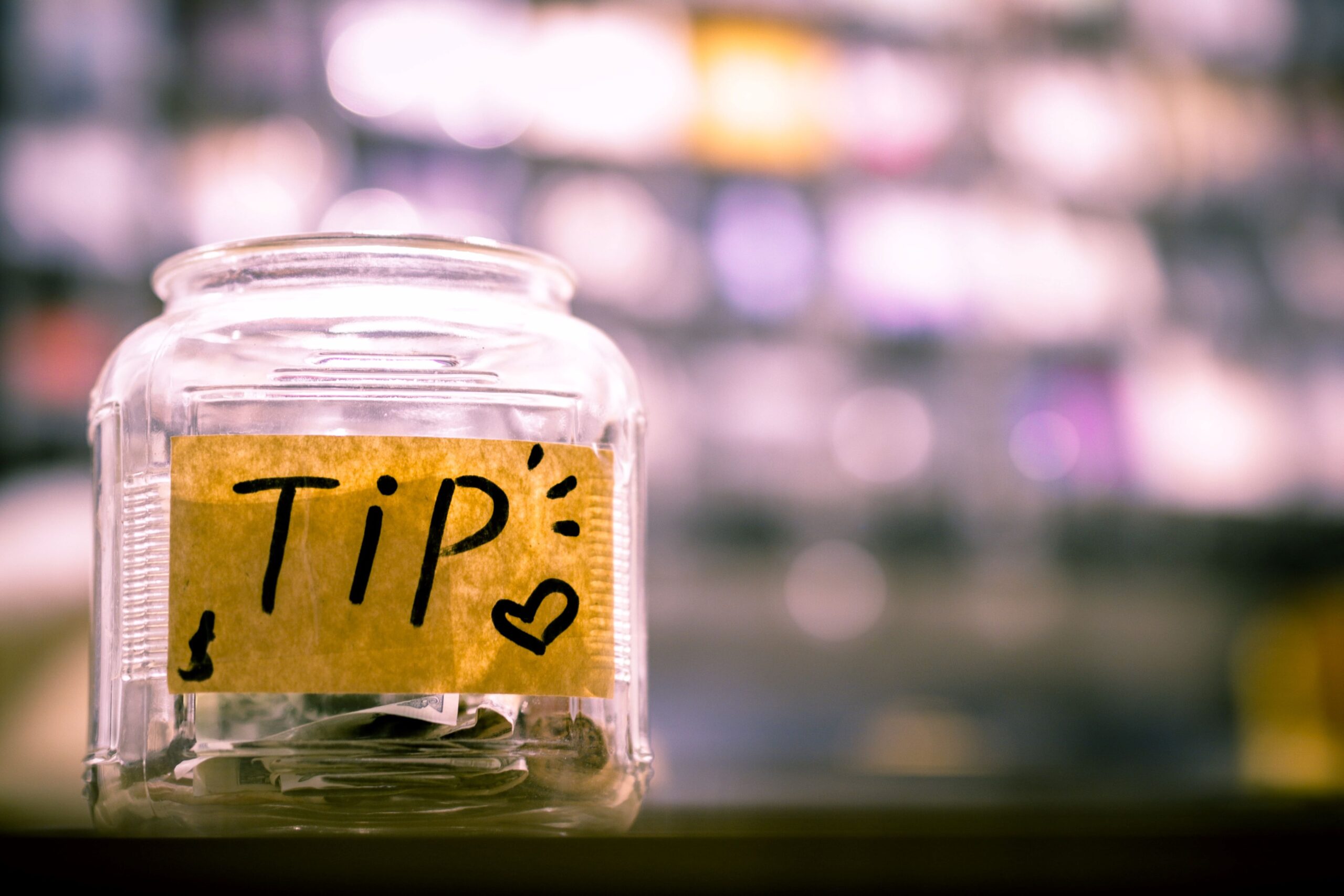 A jar filled with cash on a counter with a yellow label on it that says "Tip".