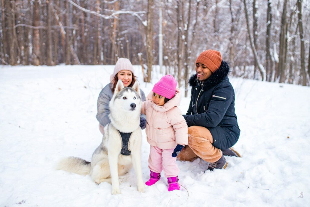 family of father, mother and daughter and dog enjoying the winter and playing in the snow